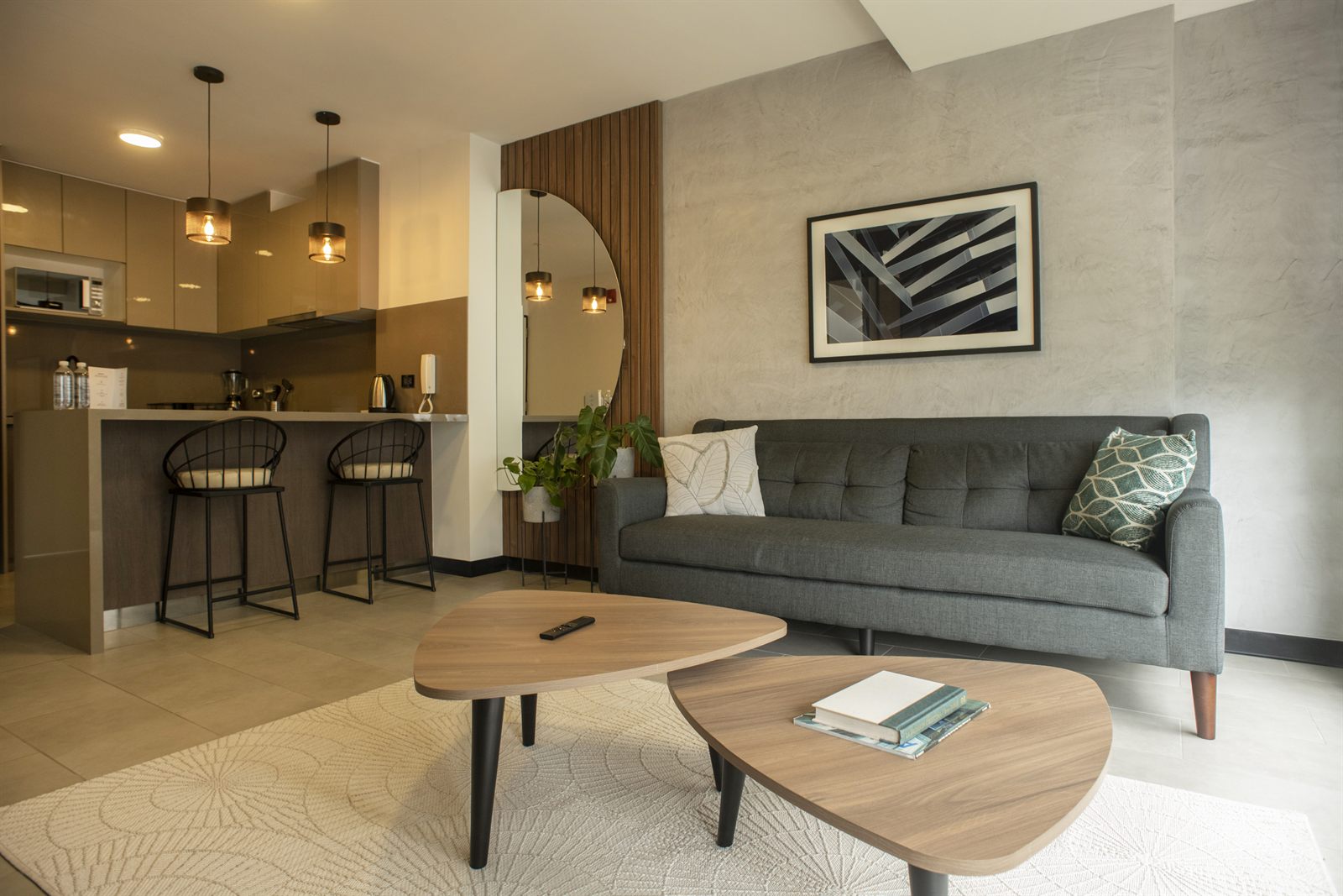 Sala y cocina de un departamento en San Isidro con pared de microcemento, sofá gris, barra con banquetas negras y listones de madera