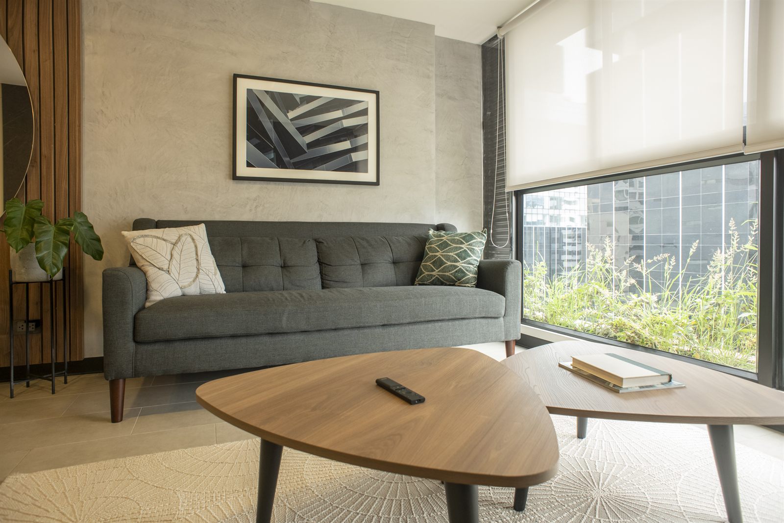 Sala de un departamento en San Isidro con sofá gris, cuadro abstracto en blanco y negro y ventanal con vegetación