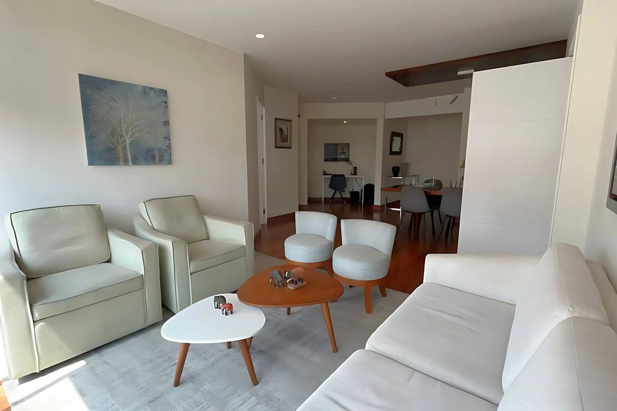 Sala y comedor de un departamento en Miraflores con sofá y sillones claros, mesas de centro de madera y escritorio al fondo