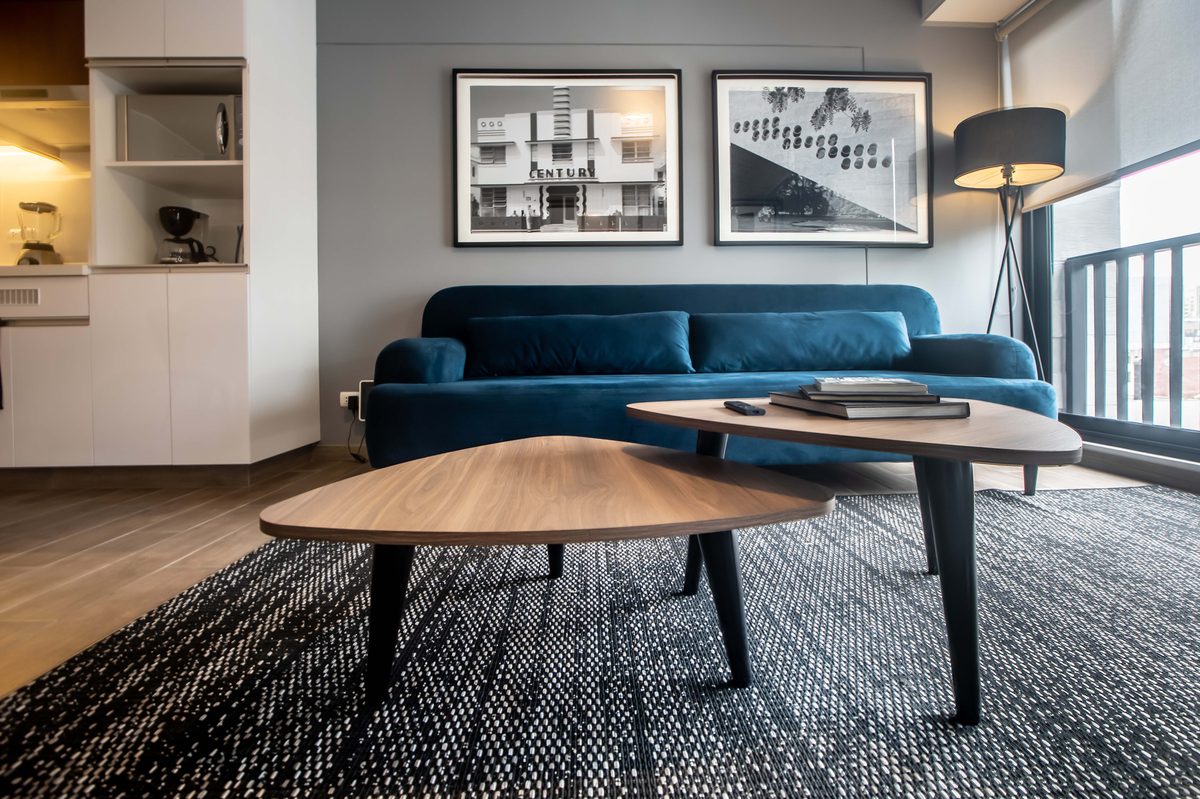 Sala de un departamento en Miraflores con sofá de terciopelo azul, mesas de centro de madera, cuadros en blanco y negro y balcón