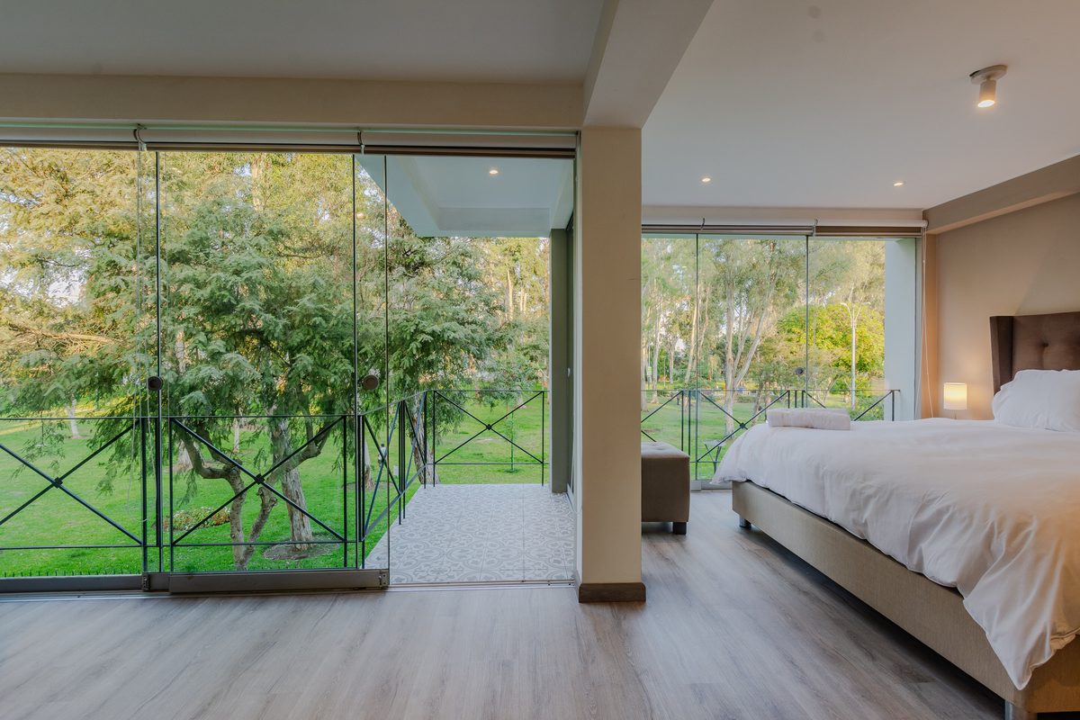 Dormitorio en San Isidro con cama de sábanas blancas y ventanales de piso a techo con vista a un parque arbolado